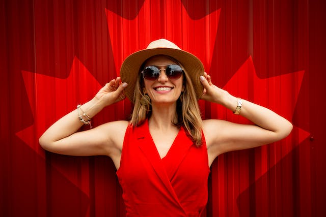 femme souriante avec chapeau et lunette de soleil et drapeau canadien rouge derrière elle