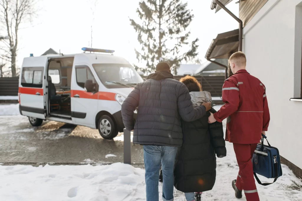 ambulancier qui aide une personne soutenue par une autre à marcher pour rentrer dans une ambulance
